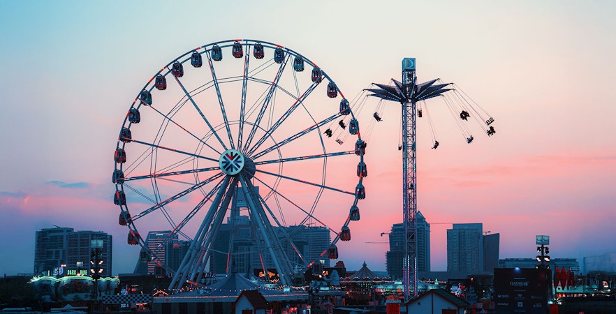 Ferris wheel and swing ride at Lusail Winter Wonderland during sunset.