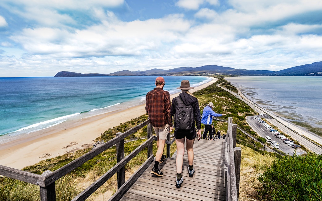 Tour group walking on Bruny Island boardwalk with ocean view and lighthouse in background.