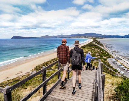 Tour group walking on Bruny Island boardwalk with ocean view and lighthouse in background.