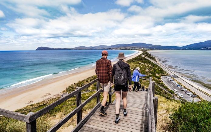Tour group walking on Bruny Island boardwalk with ocean view and lighthouse in background.