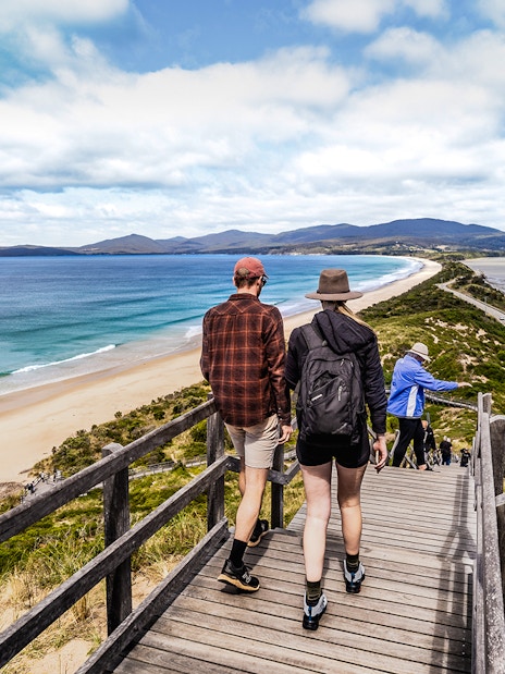 Tour group walking on Bruny Island boardwalk with ocean view and lighthouse in background.