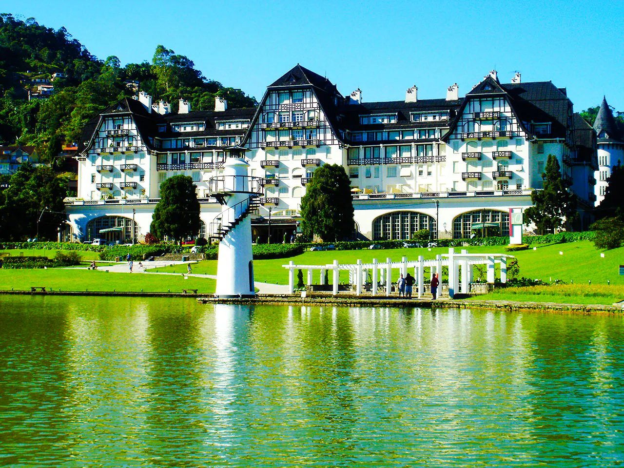 Grand hotel by a lake in Petrópolis, Rio de Janeiro, with lush gardens and a white lighthouse.