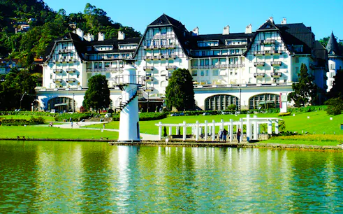 Grand hotel by a lake in Petrópolis, Rio de Janeiro, with lush gardens and a white lighthouse.