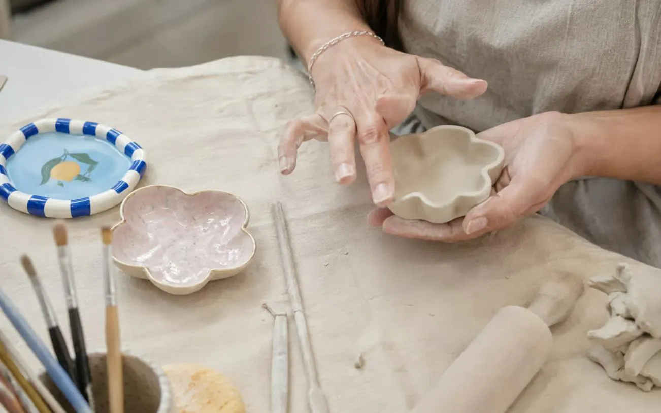 Hands shaping clay into a flower dish at a Krakow air-dry clay workshop.