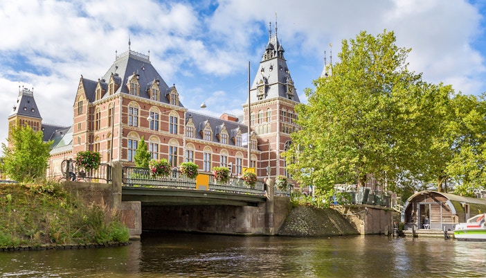 Rijksmuseum view from Amsterdam canal with bridge and trees.