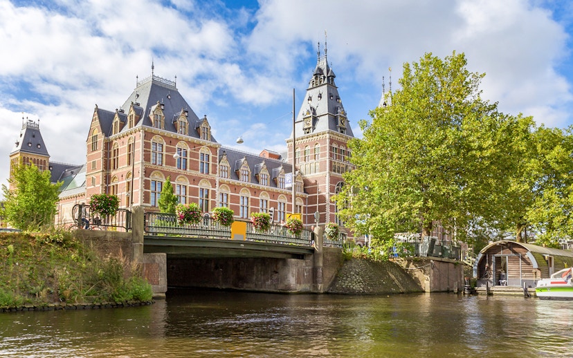 Rijksmuseum view from Amsterdam canal with bridge and trees.