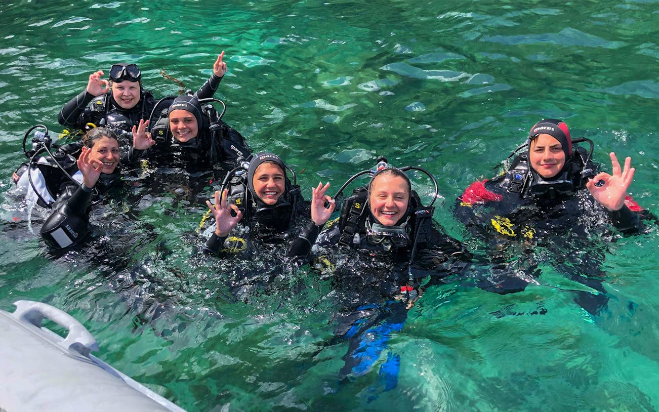Group of divers in wetsuits enjoying a scuba diving baptism in the Bosa Sea.