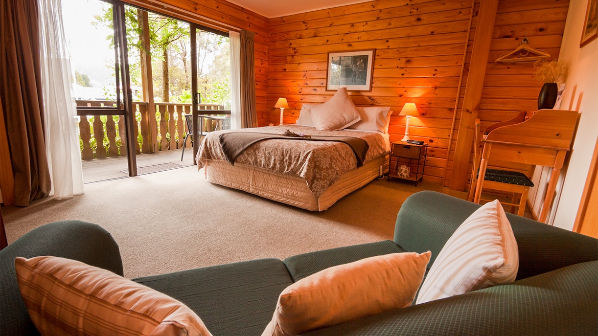 Cozy wooden cabin bedroom with a double bed and balcony view in Queenstown, New Zealand.