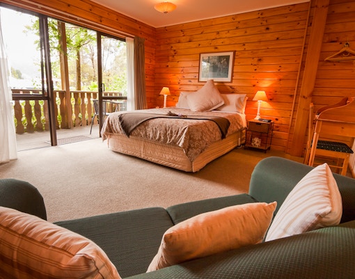 Cozy wooden cabin bedroom with a double bed and balcony view in Queenstown, New Zealand.