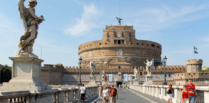 Tour group walking towards Castel Sant'Angelo in Rome, Italy, with historic statues and architecture.
