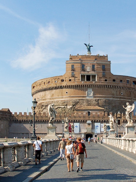 Tour group walking towards Castel Sant'Angelo in Rome, Italy, with historic statues and architecture.