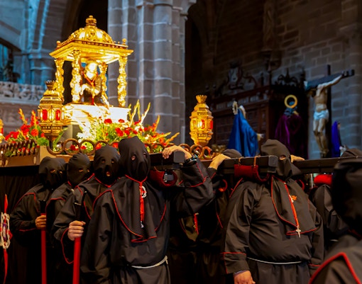 Procession during Semana Santa in Ávila with hooded participants carrying a religious float.