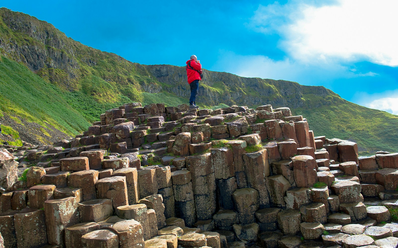 Man standing on basalt columns at Giant's Causeway trail, Northern Ireland.