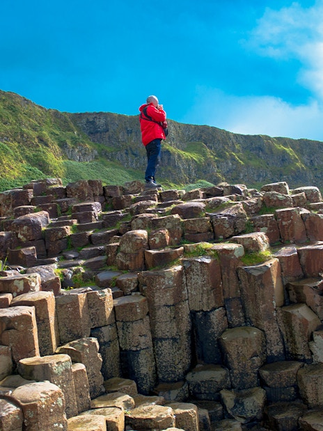 Man standing on basalt columns at Giant's Causeway trail, Northern Ireland.