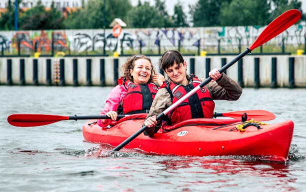 Two people kayaking on a private tour near a graffiti-covered wall.