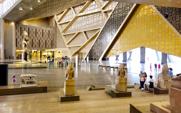 Grand Egyptian Museum interior with ancient statues and visitors in Cairo.