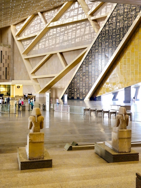 Grand Egyptian Museum interior with ancient statues and visitors in Cairo.