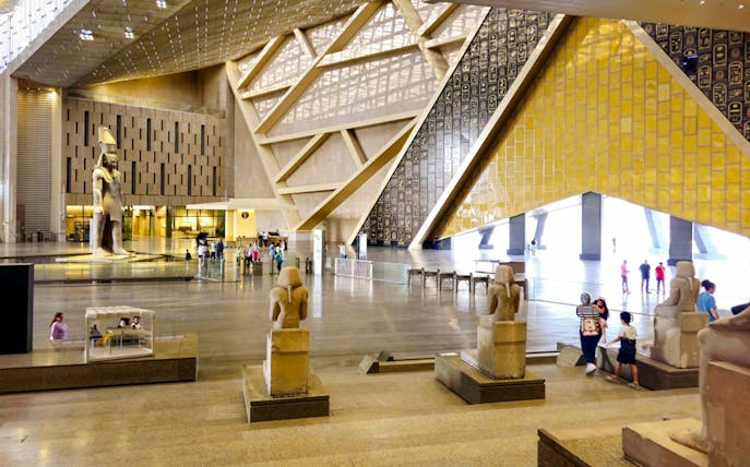 Grand Egyptian Museum interior with ancient statues and visitors in Cairo.
