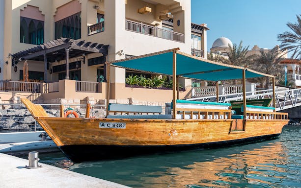 Traditional wooden boat moored in Abu Dhabi harbour near modern architecture.