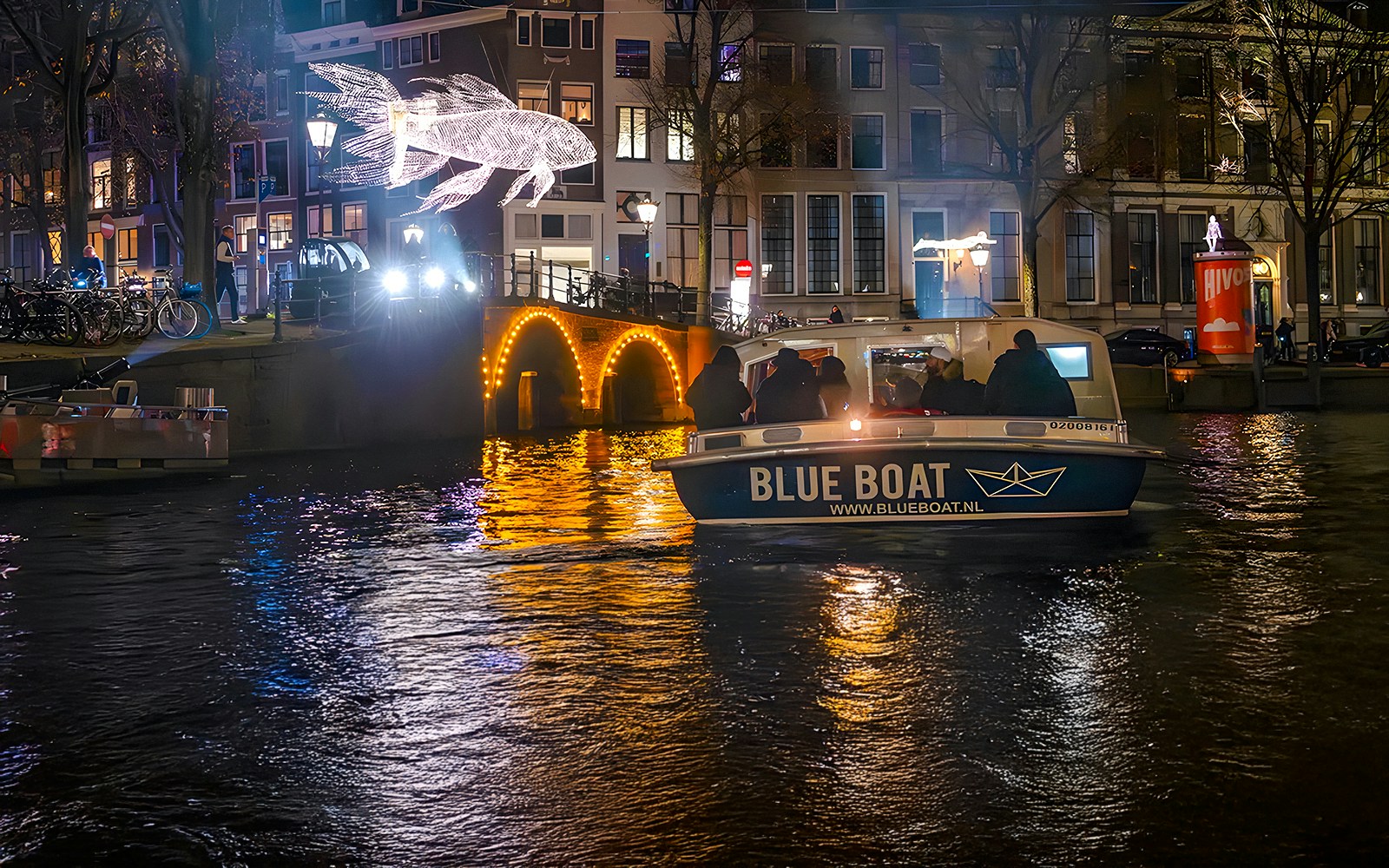Amsterdam Light Festival cruise boat passing illuminated canal bridge and light sculpture.