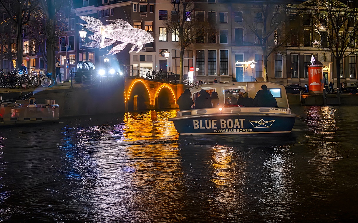 Amsterdam Light Festival cruise boat passing illuminated canal bridge and light sculpture.