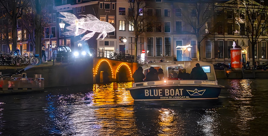 Amsterdam Light Festival cruise boat passing illuminated canal bridge and light sculpture.