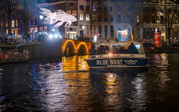 Amsterdam Light Festival cruise boat passing illuminated canal bridge and light sculpture.