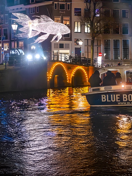 Amsterdam Light Festival cruise boat passing illuminated canal bridge and light sculpture.