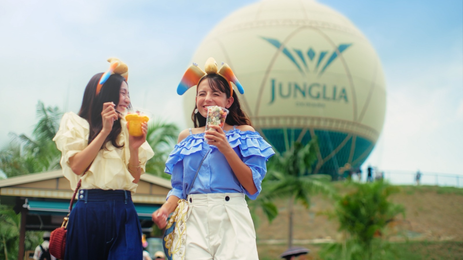 Visitors enjoying snacks at JUNGLIA OKINAWA Park with the park's balloon in the background.