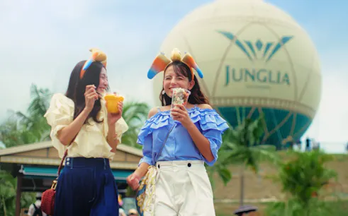 Visitors enjoying snacks at JUNGLIA OKINAWA Park with the park's balloon in the background.