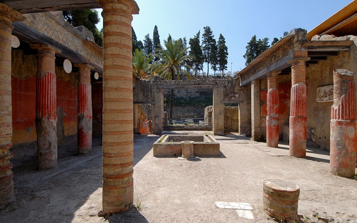 Ruins of Casa del Rilievo di Telefo in Herculaneum with red columns and ancient courtyard.