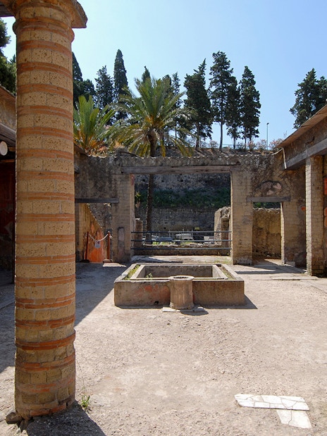 Ruins of Casa del Rilievo di Telefo in Herculaneum with red columns and ancient courtyard.