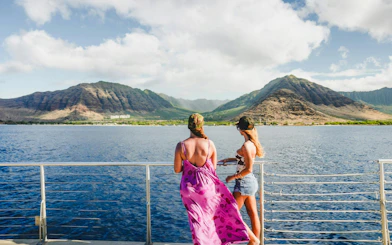 Two people on a boat enjoying the view of mountains in West Oahu during a whale watch sail.