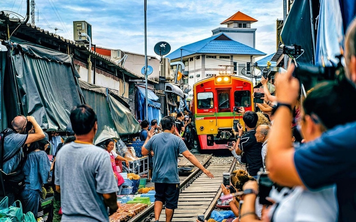 Tourists at Maeklong Train Market in Bangkok as train passes through stalls.