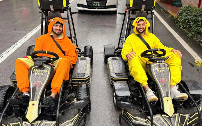 Two people in colorful costumes driving go-karts on Asakusa street during a 60-minute tour.