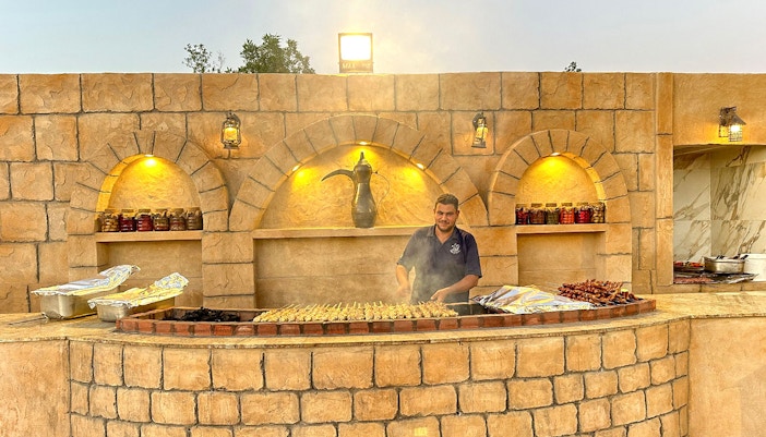 Grill chef preparing skewers at a desert safari barbecue station.