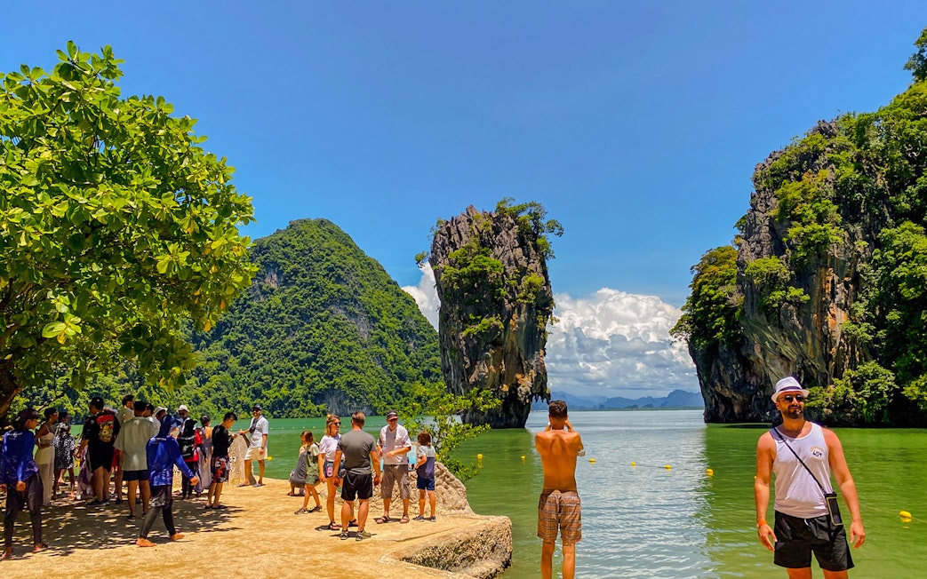 Tourists exploring James Bond Island with limestone cliffs in Phang Nga Bay, Thailand.