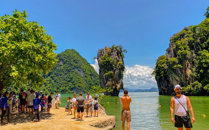 Tourists exploring James Bond Island with limestone cliffs in Phang Nga Bay, Thailand.