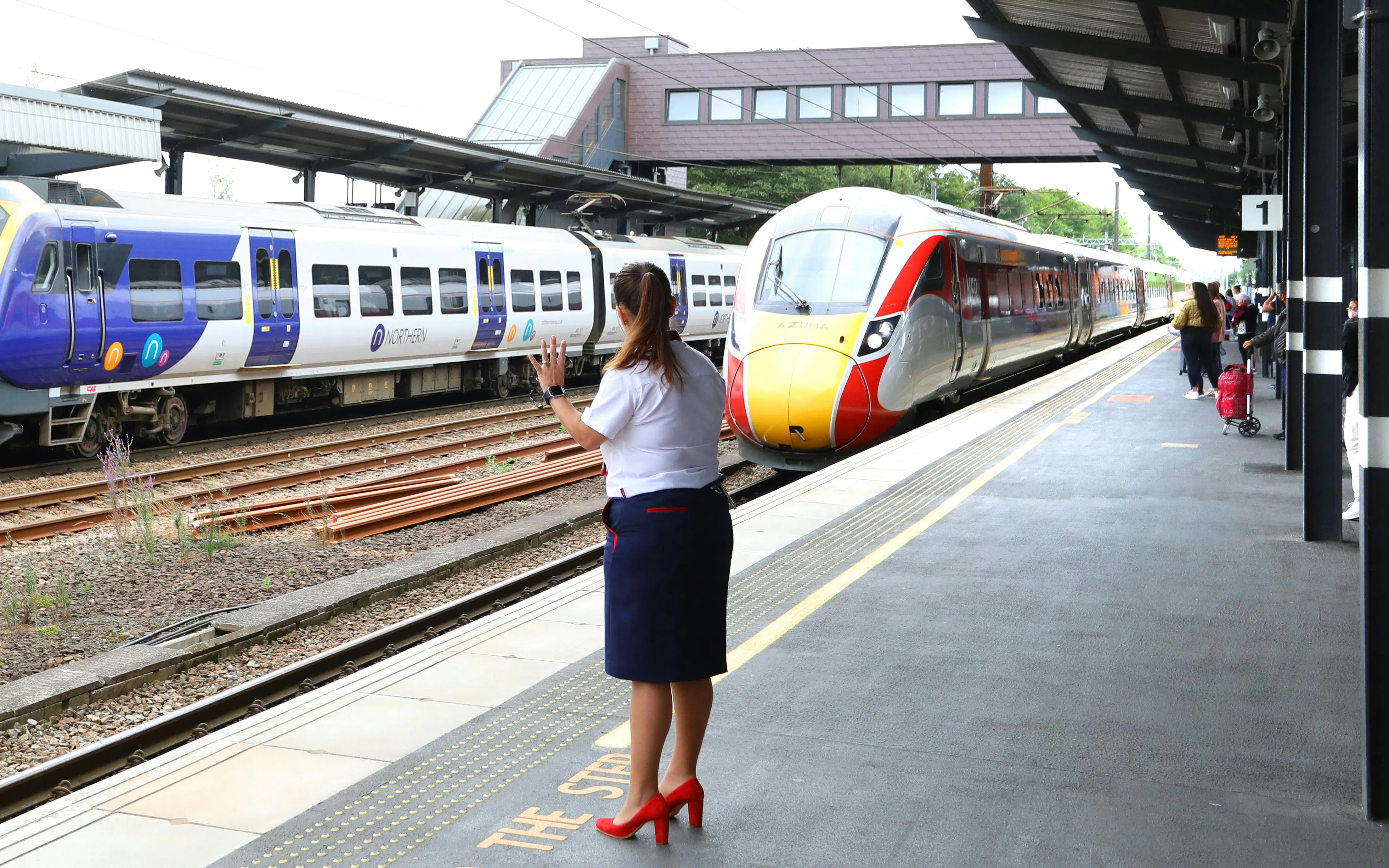 Train arriving at a station on the National Rail network in England, with a conductor on the platform.