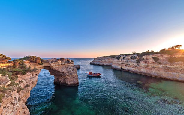 Boat exploring coastal caves during X Ride Dolphin and Caves Tour at sunset.