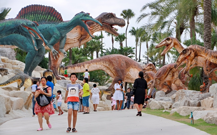 Visitors walking among dinosaur sculptures at Nong Nooch Tropical Garden, Thailand.
