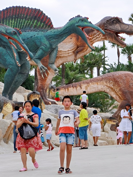 Visitors walking among dinosaur sculptures at Nong Nooch Tropical Garden, Thailand.
