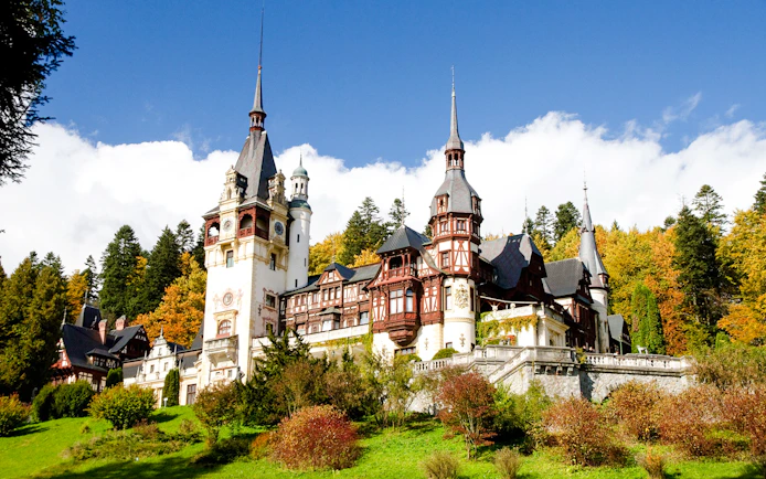 Peleș Castle in Romania surrounded by autumn trees.