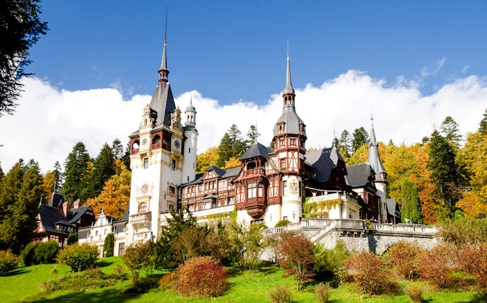 Peleș Castle in Romania surrounded by autumn trees.