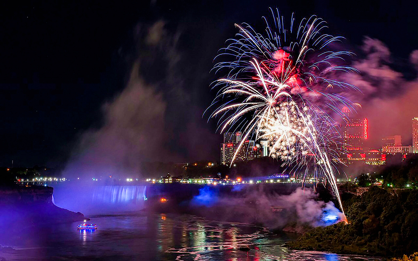 Fireworks display over Niagara Falls at night with city lights in the background.