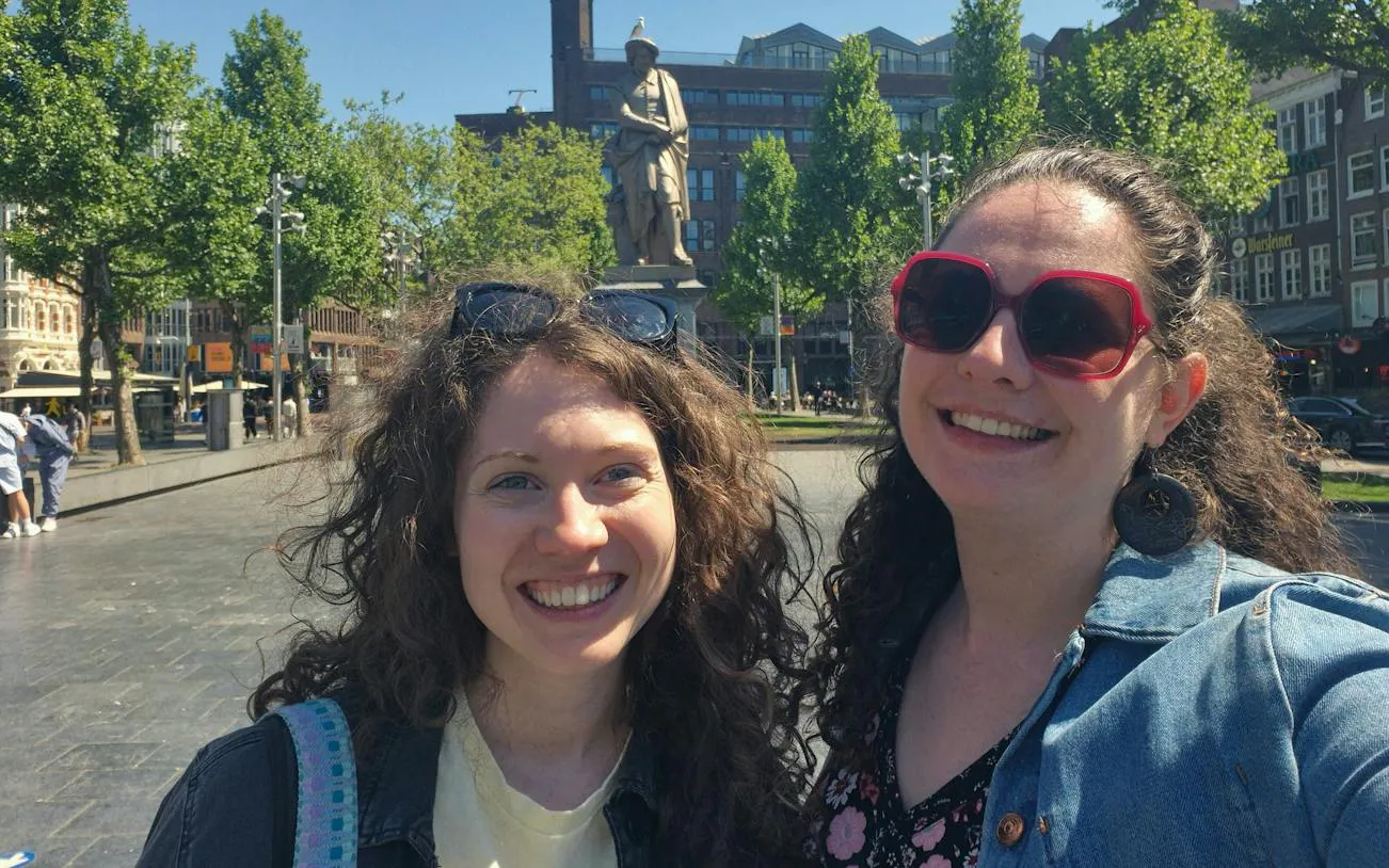 Two people smiling in front of Rembrandt statue in Amsterdam during a city exploration game.