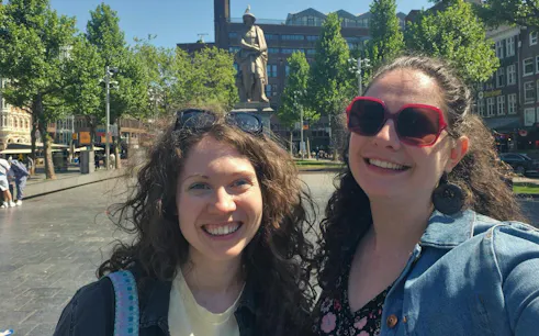 Two people smiling in front of Rembrandt statue in Amsterdam during a city exploration game.