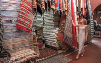 Woman browsing colorful traditional rugs in a Taroudant market.