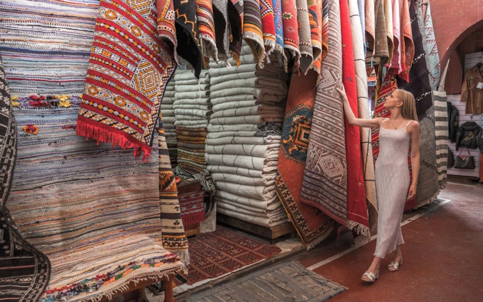 Woman browsing colorful traditional rugs in a Taroudant market.