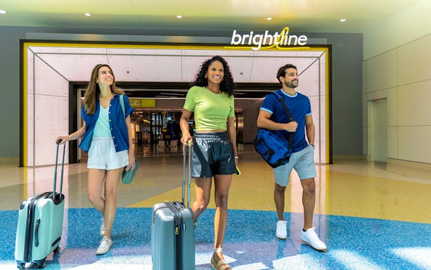 Travelers with luggage at Brightline station, Miami to Orlando route.